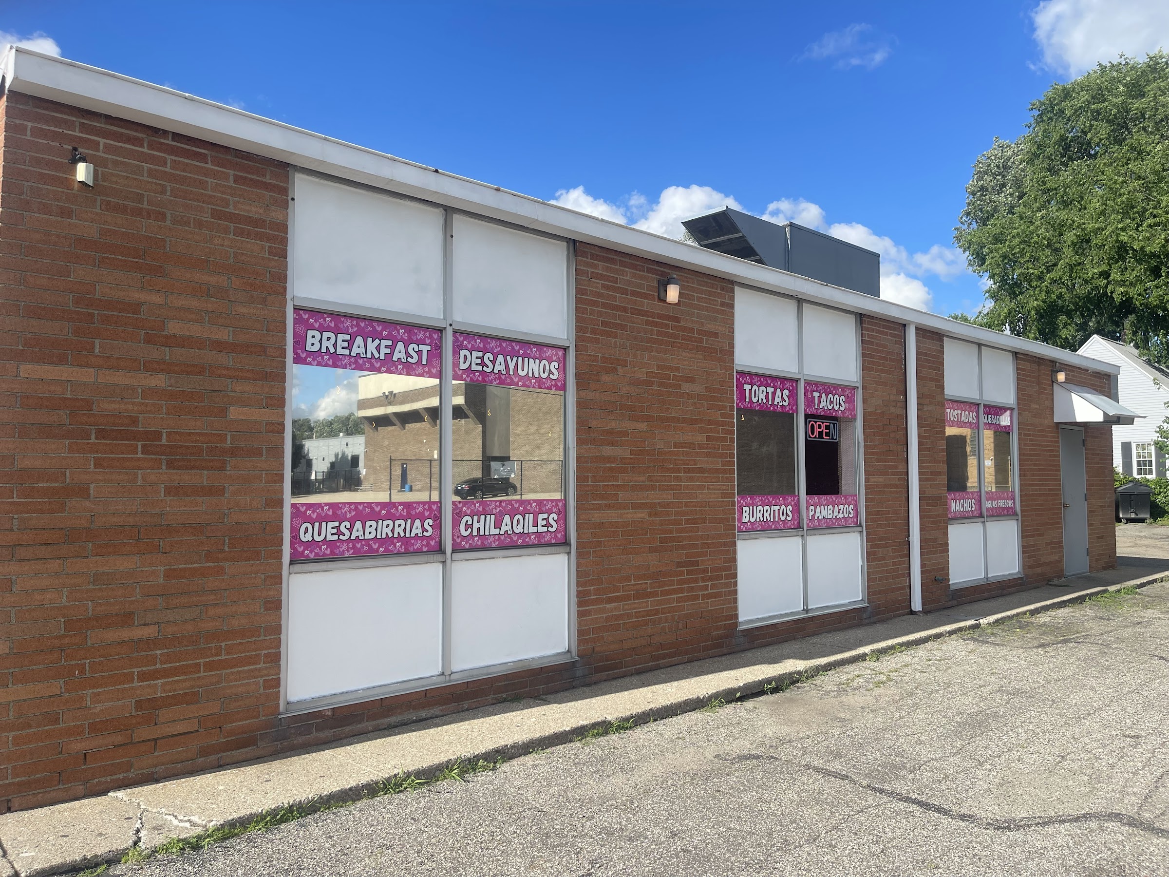 The long brick storefront with hot-pink window decals listing breakfast, quesabirrias and tacos