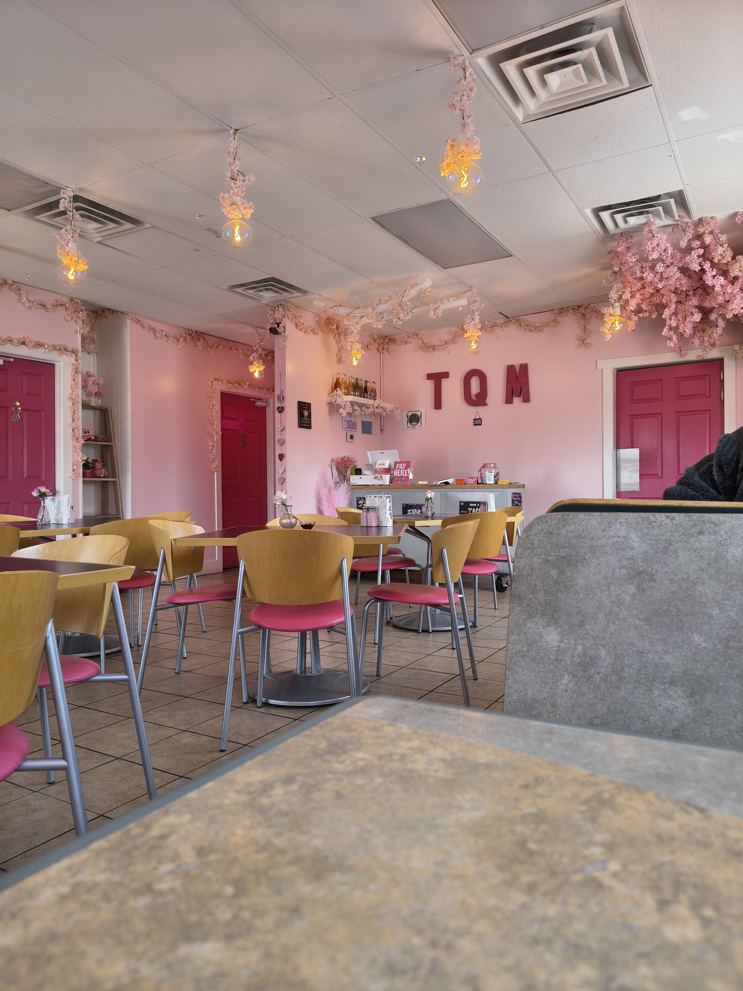 The full pink dining room with yellow-and-pink chairs and the TQM monogram on the wall